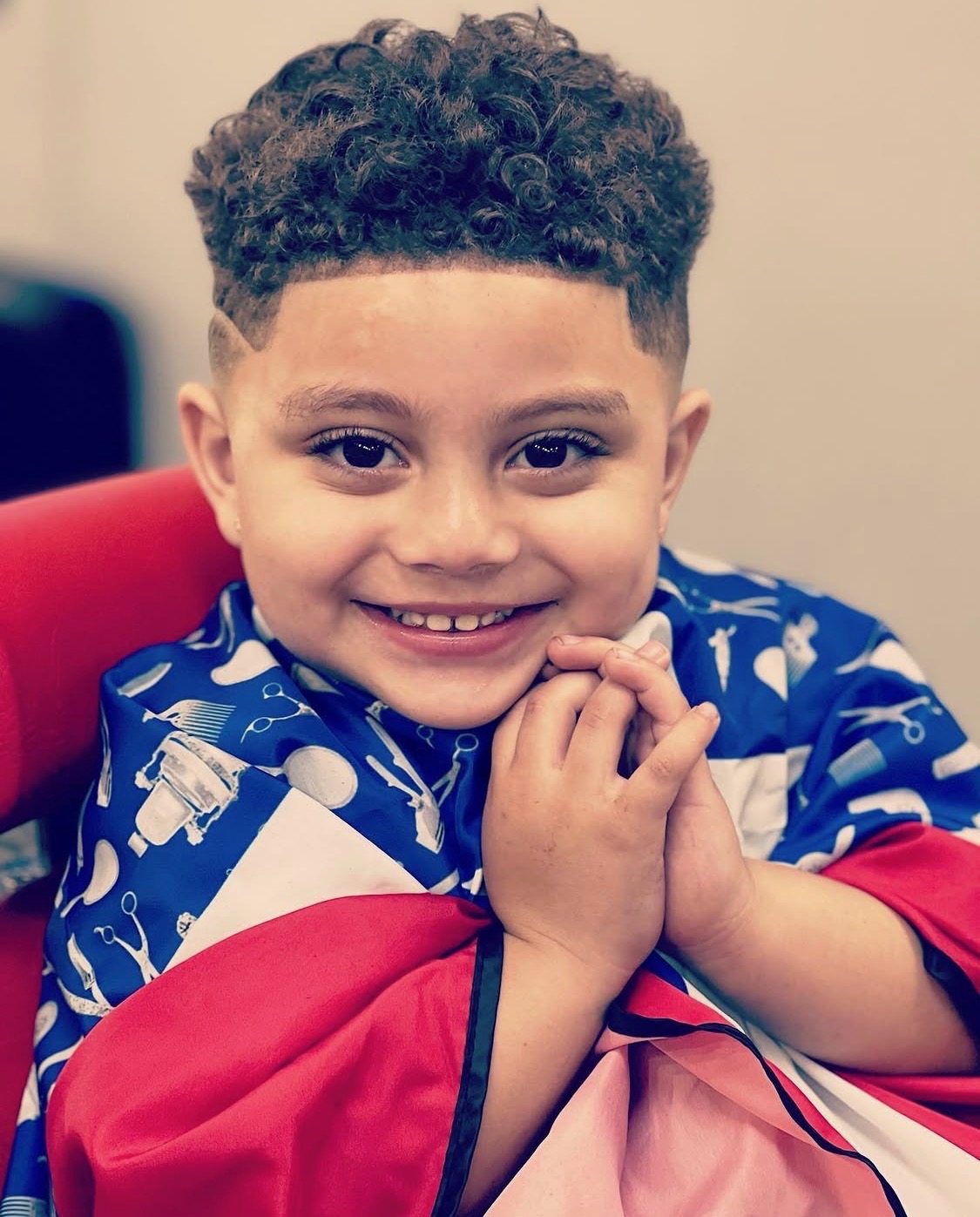Smiling kid with curly fade in barber cape — X Express Barbershop